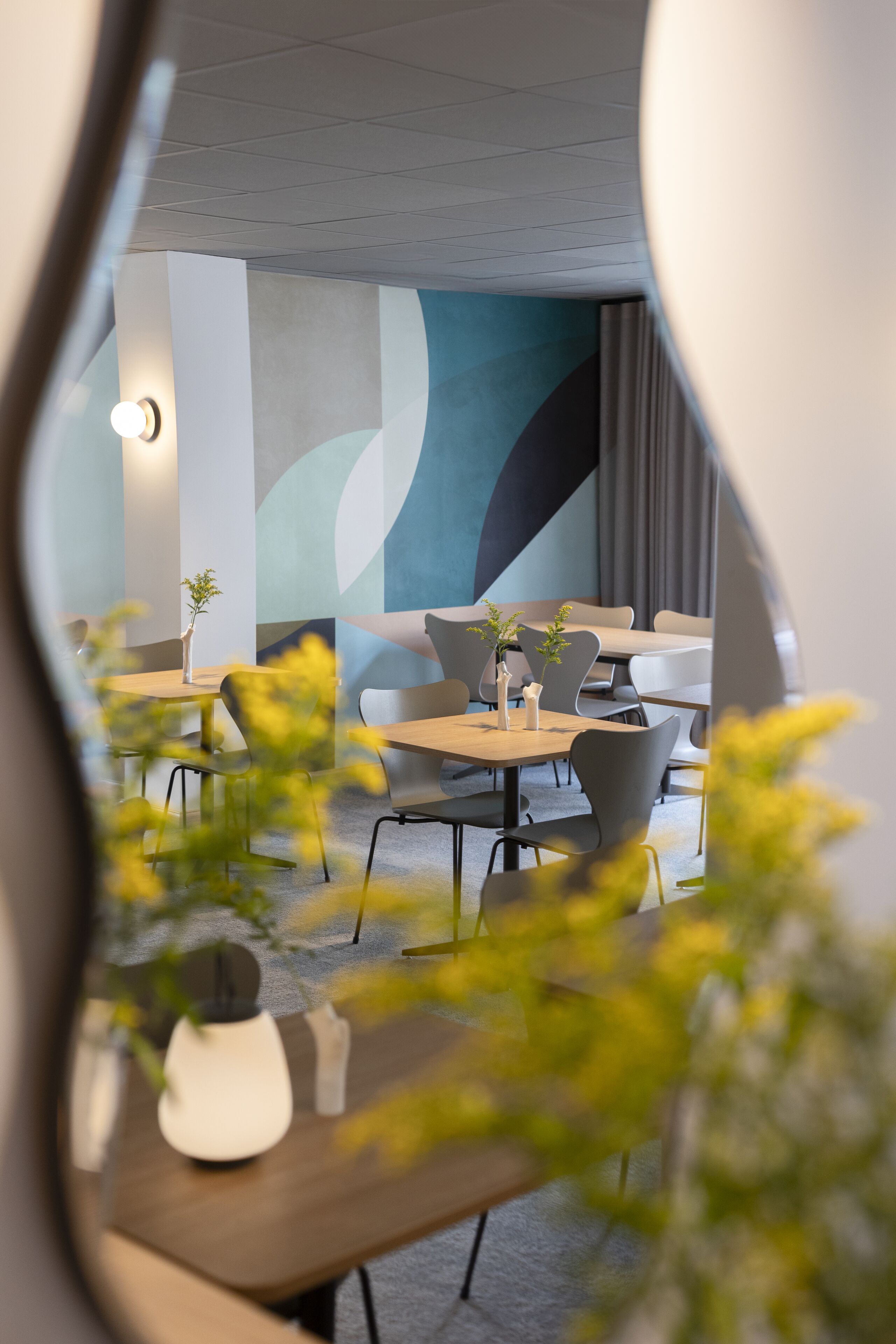 Un comedor moderno con mesas y sillas, un muro decorativo y una planta sobre la mesa.