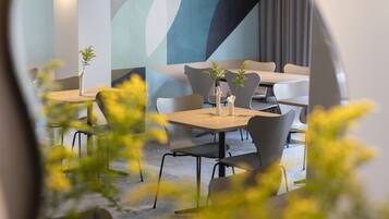 Un comedor moderno con mesas y sillas, un muro decorativo y una planta sobre la mesa.