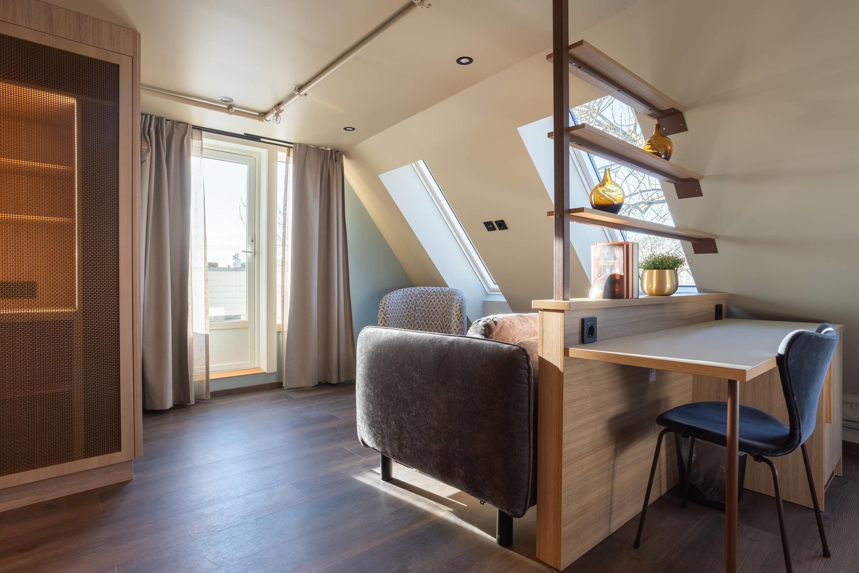 A modern loft bedroom with a sloped ceiling, skylight, built-in desk, and a cozy seating area.