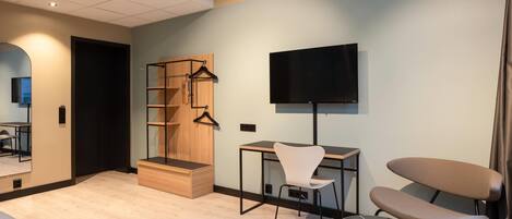 A modern hotel room with a wooden desk, a chair, a TV mounted on the wall, and a small seating area with a cushioned bench.