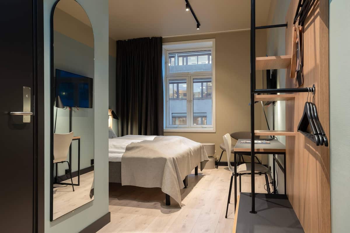Ein modernes Hotelzimmer mit Bett, Schreibtisch, Stuhl und einem großen Spiegel.