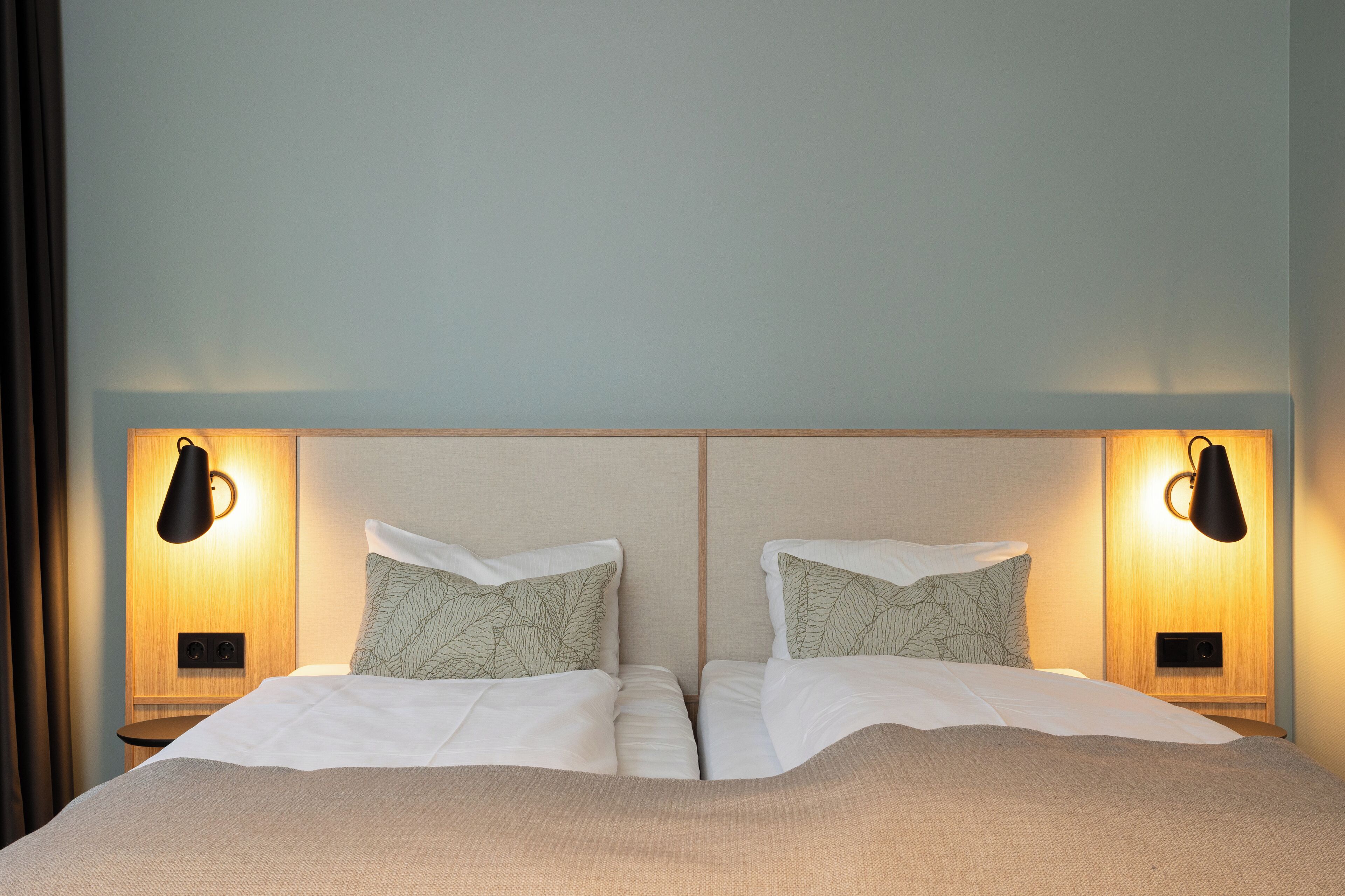 A double bed with a wooden headboard, two bedside lamps, and patterned pillows.