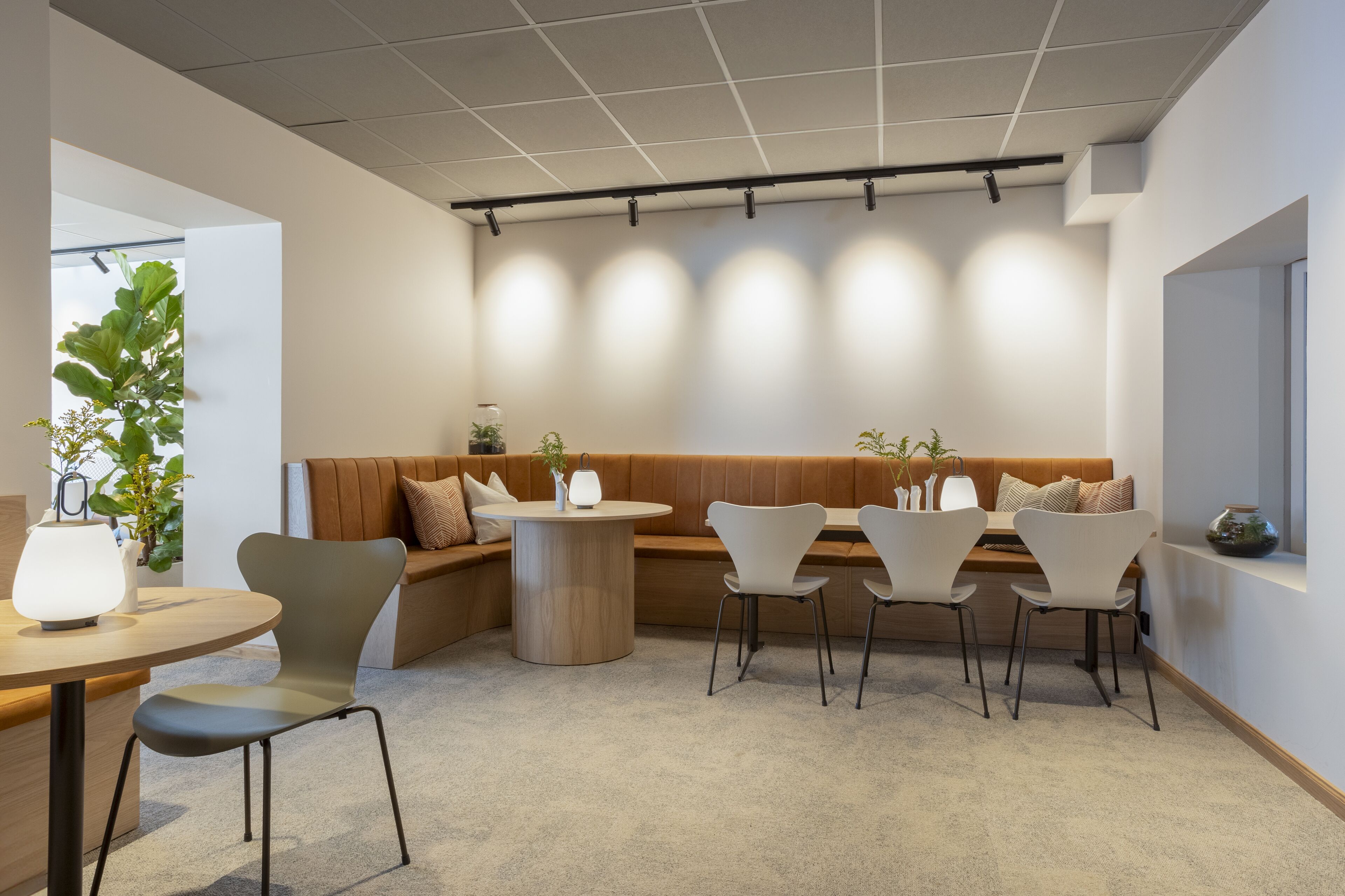 Un área de estar moderna con un banco de madera, sillas blancas y una mesa redonda.
