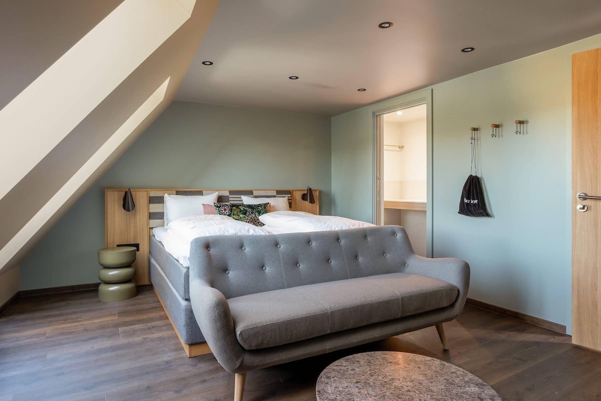 Ein modernes Schlafzimmer mit einem Bett, einem grauen Sofa, einem runden Tisch und einem Holz-Kopfteil.