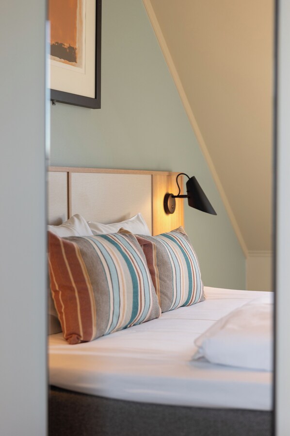 A neatly made bed with striped pillows, a headboard, and a wall-mounted lamp. - Comfort Hotel Park (Trondheim)