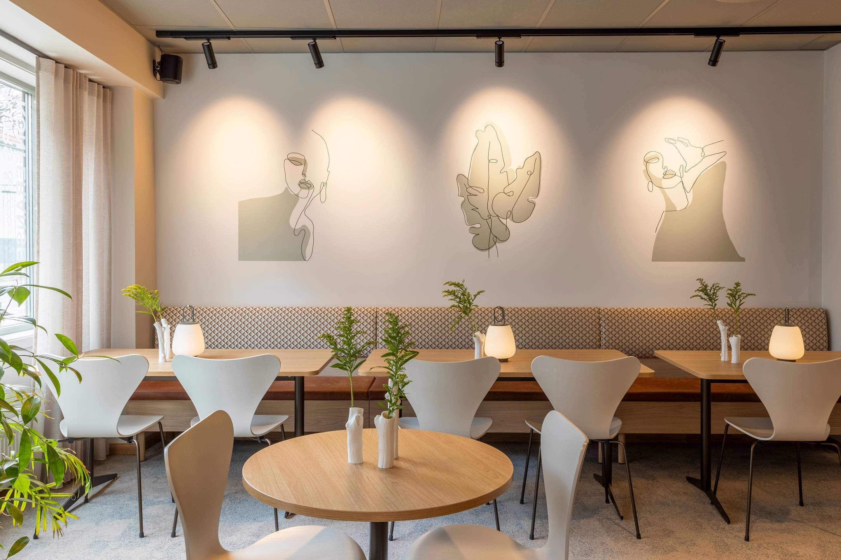 Un restaurante moderno con sillas blancas, mesas redondas y cuadros en la pared.