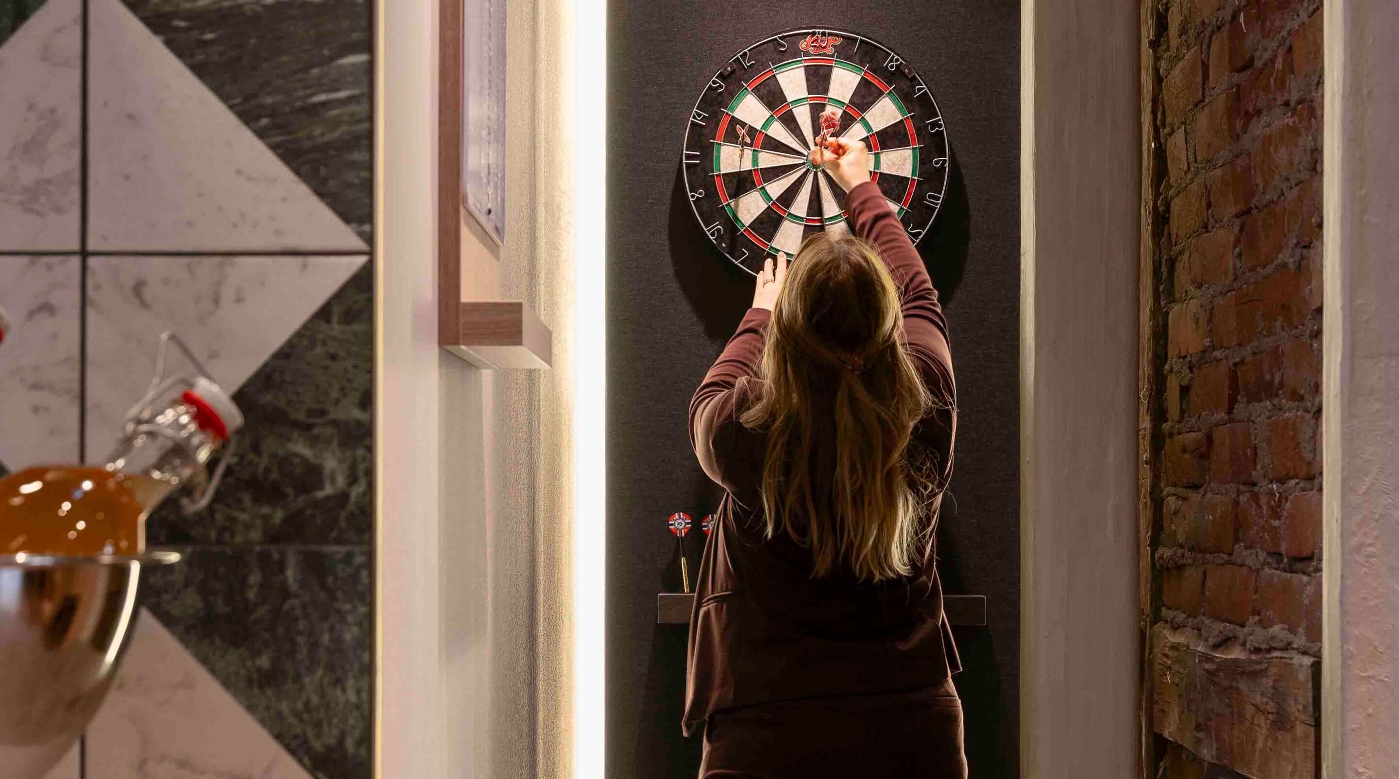A person playing darts at a wall-mounted dartboard.