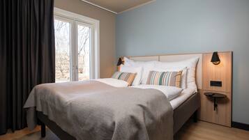 A bedroom with a bed, curtains, a nightstand, and a wall-mounted lamp.