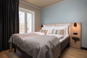A bedroom with a bed, curtains, a nightstand, and a wall-mounted lamp.