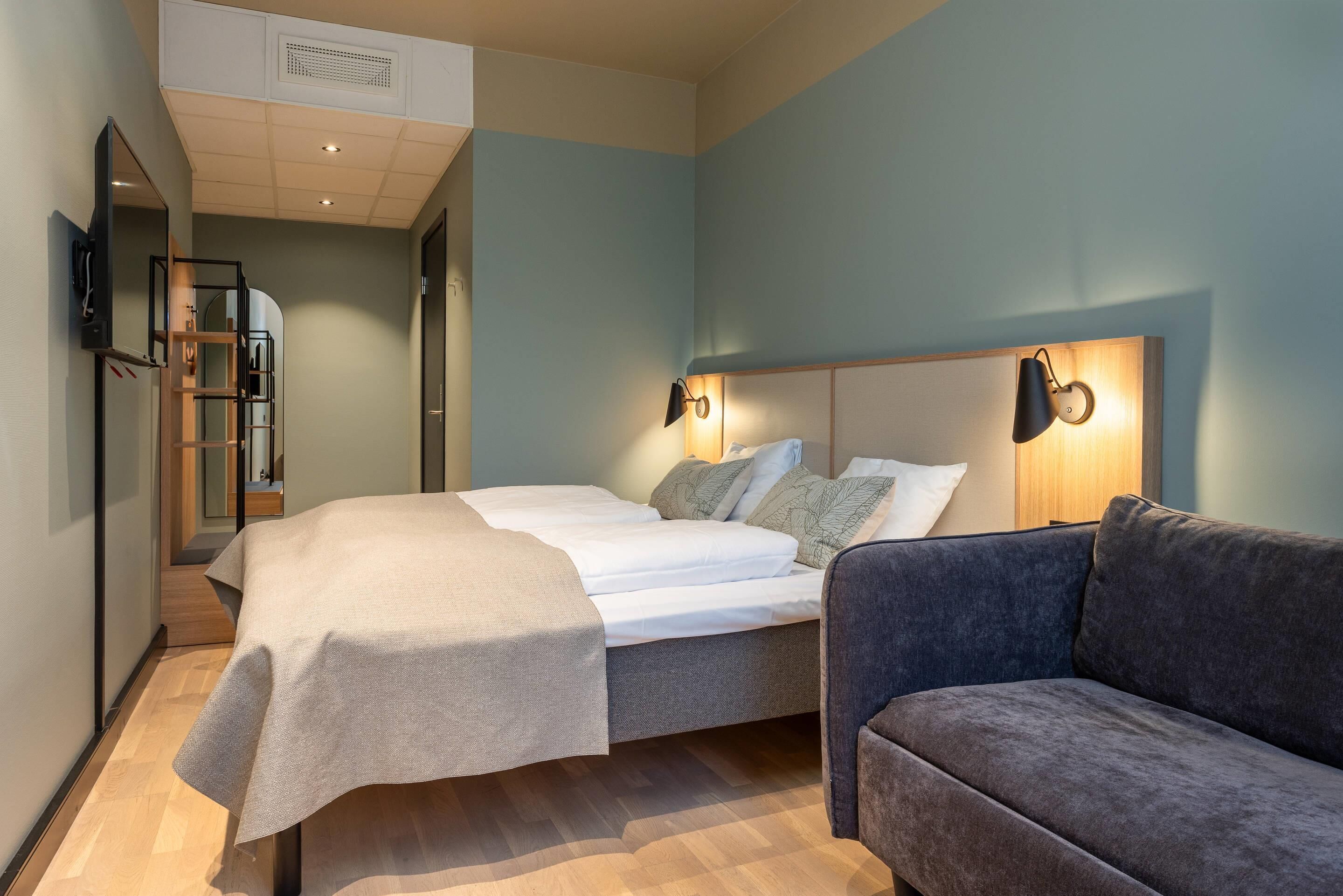 A modern bedroom with a bed, a sofa, and a TV mounted on the wall.