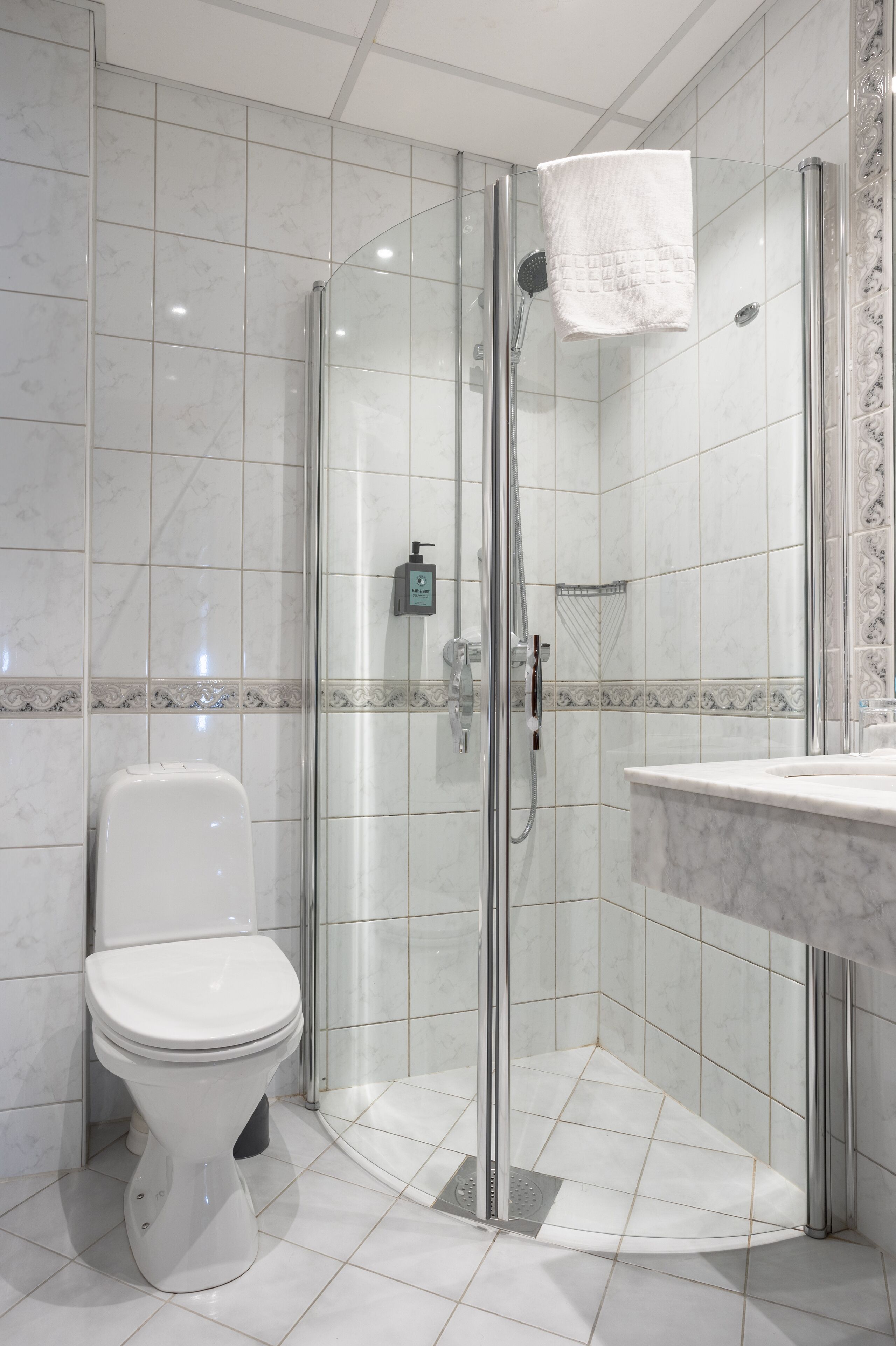 A modern bathroom with a glass-enclosed shower, a white toilet, and a marble-tiled floor.