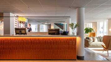 A reception area with a modern design, featuring a reception desk, a bar area, and a seating area with a sofa and chairs.
