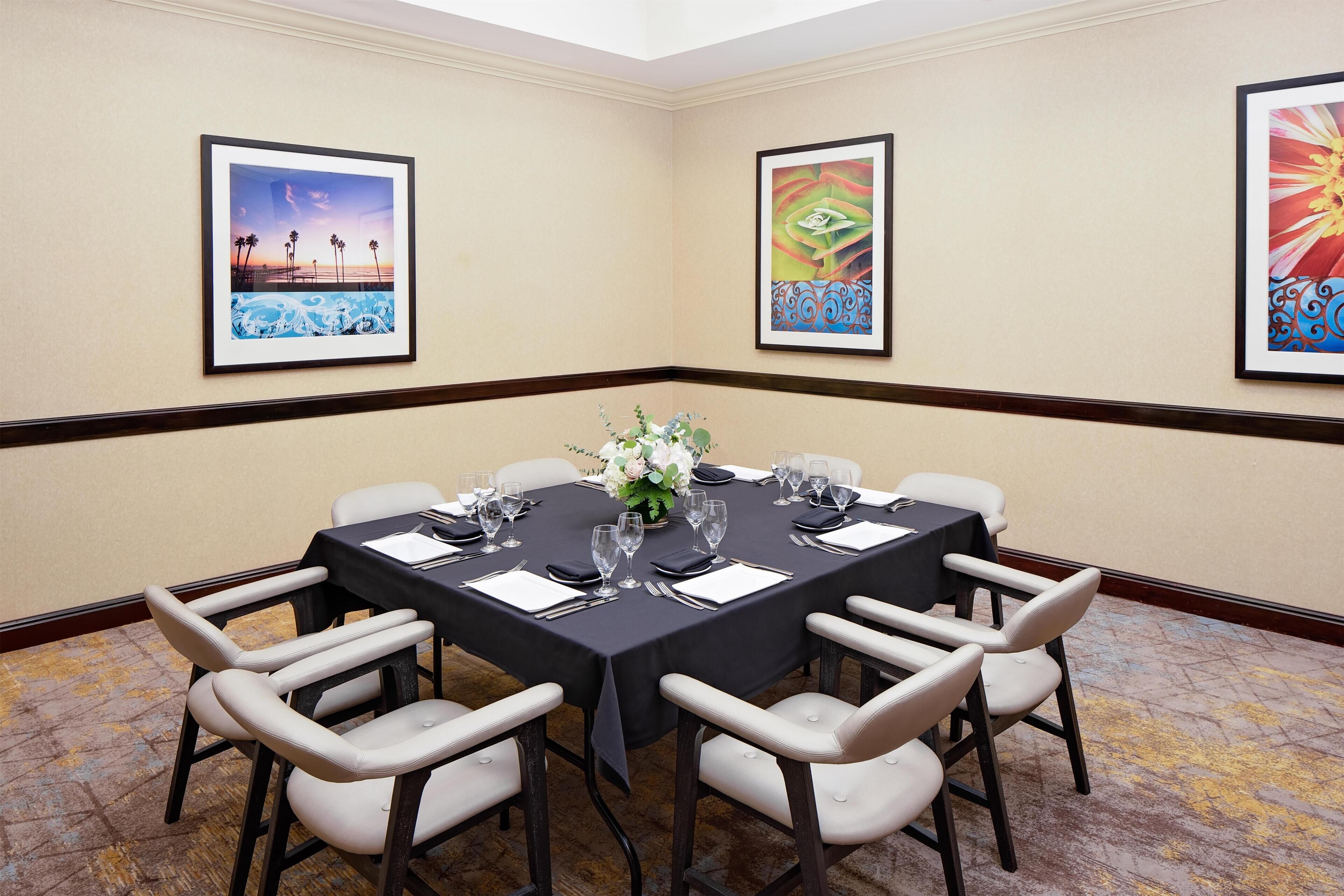 A conference room with a round table, white chairs, and framed artwork on the walls.