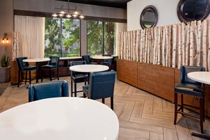A restaurant interior with round tables, blue chairs, a wooden wall, and large windows.