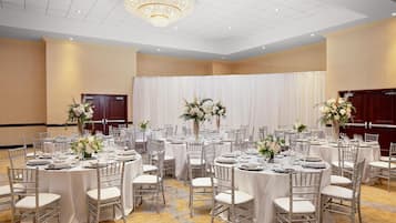 A banquet hall with round tables, white tablecloths, and silver chairs.