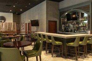 A bar area with a long counter, green chairs, and a television mounted on the wall. - Hotel Zessa Orange County Airport, a DoubleTree by Hilton (Santa Ana)