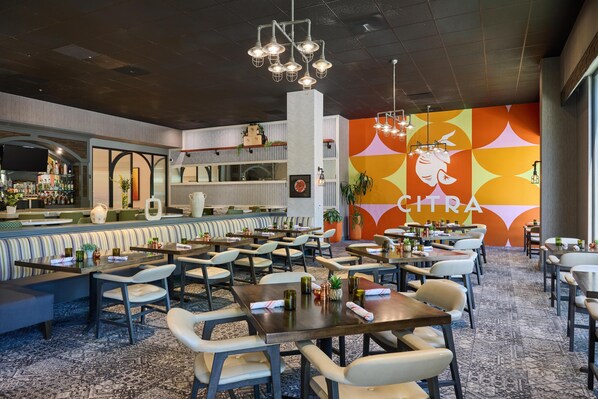 Un restaurante con varias mesas y sillas, una zona de bar y una pared colorida con la palabra 'CHIRA' a la vista.