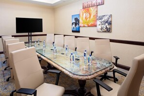 A conference room with a glass table, beige chairs, a flat-screen TV, and artwork on the walls. - Hotel Zessa Orange County Airport, a DoubleTree by Hilton (Santa Ana)
