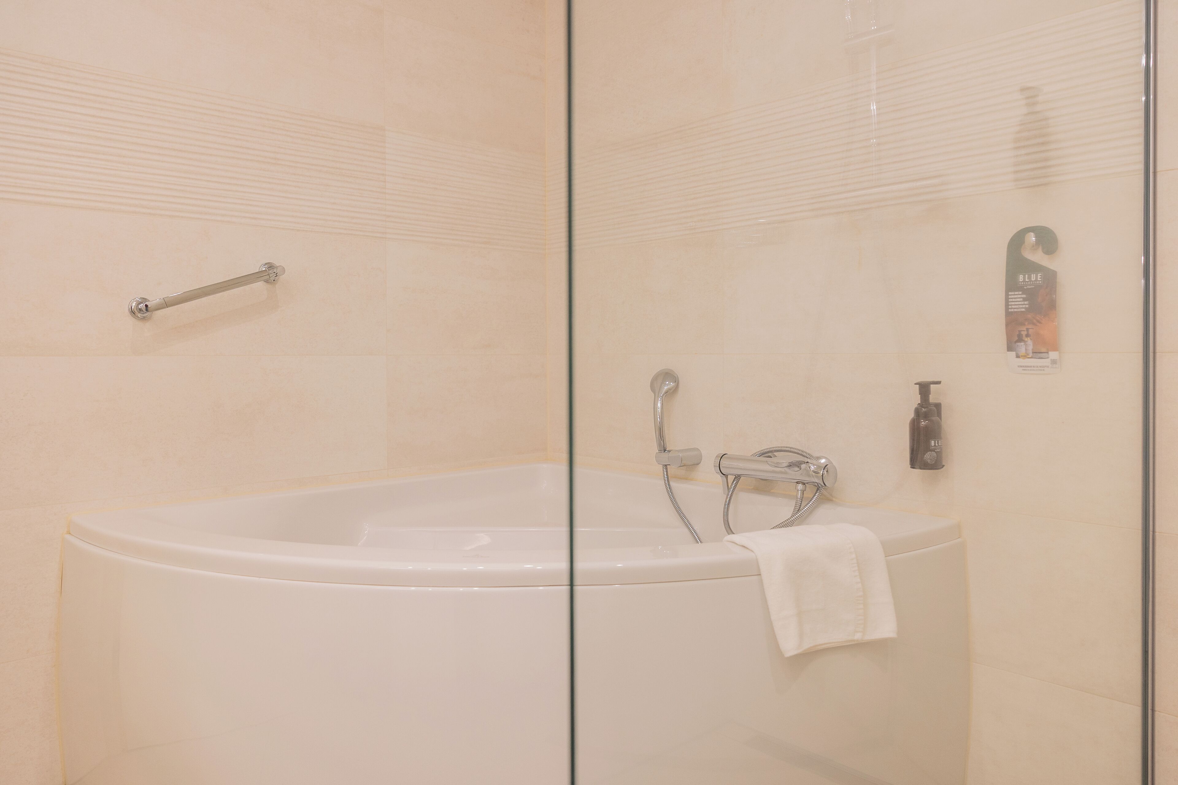 A modern bathroom with a glass-enclosed bathtub, a handheld showerhead, and a towel rack.