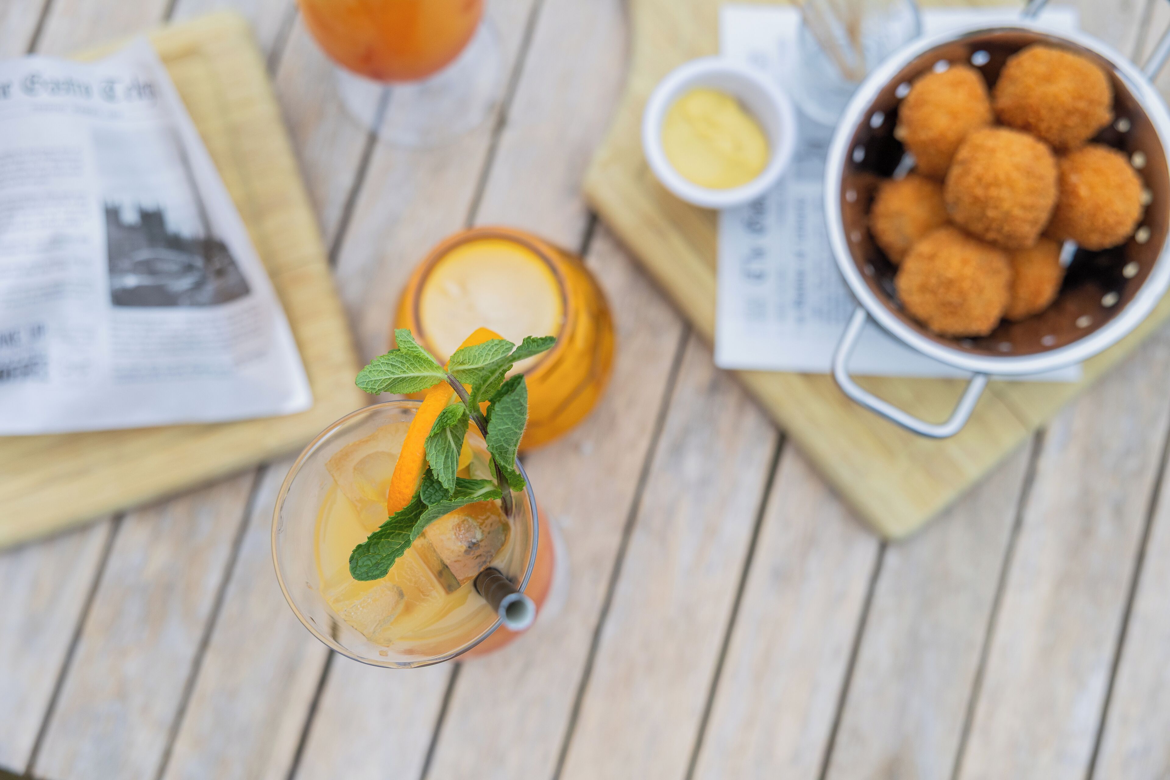 Een tafel met een glas verfrissend drankje, versierd met munt, een kaars en een schaal met gebakken snacks.