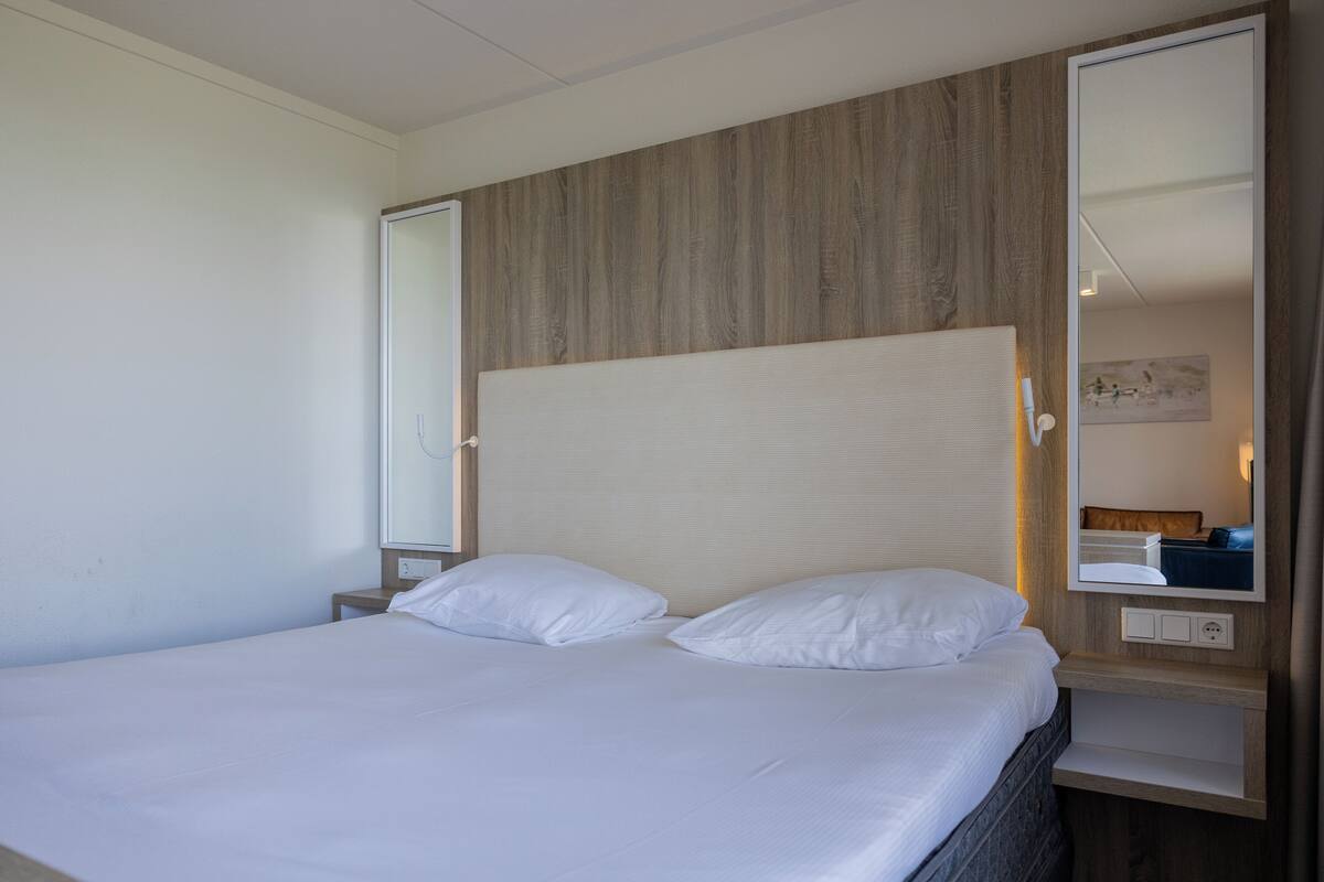 A hotel room with a bed, a nightstand, a mirror, and a wooden headboard.