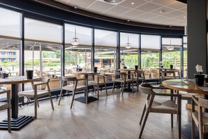 Un café amplio con ventanas grandes, mesas de madera y sillas de mimbre.
