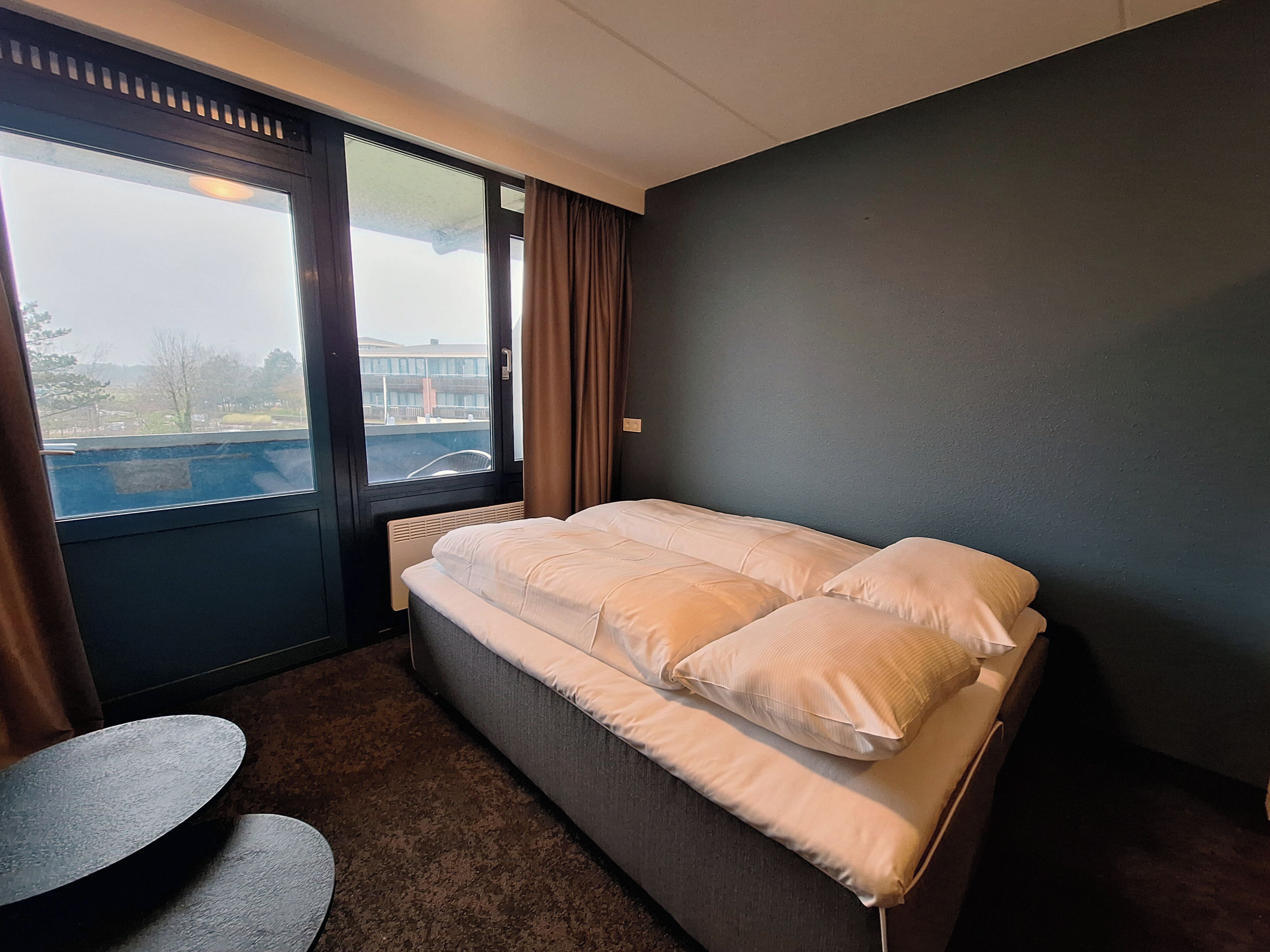 Et hotelværelse med en stor seng, et lille rundt bord og udsigt ud ad et vindue.
