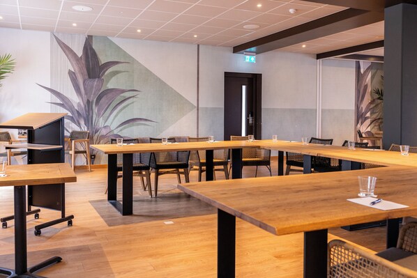 Un salón de conferencias con largas mesas y sillas, una planta grande y un diseño moderno.