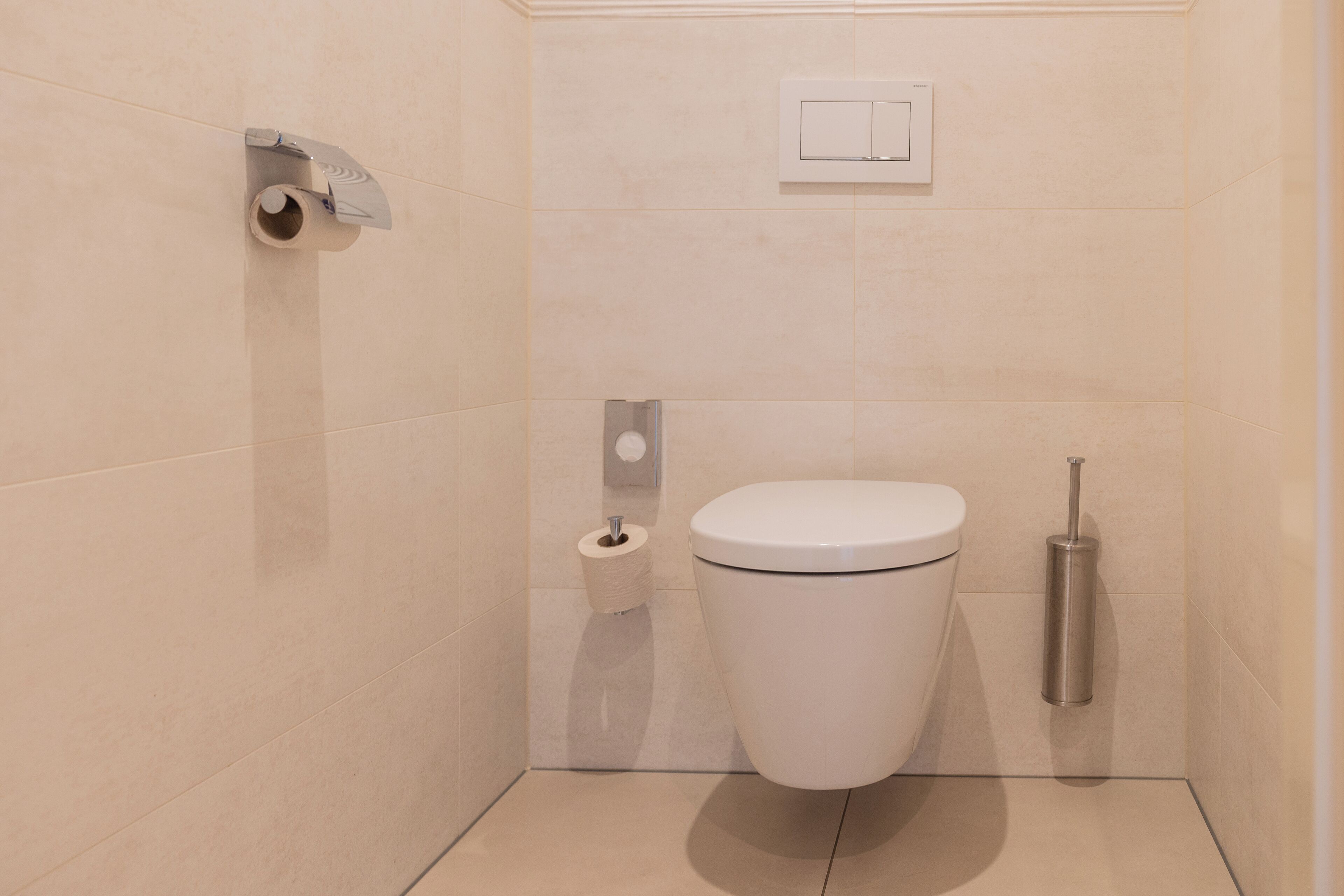 Une petite salle de bain moderne équipée de toilettes, d’un rouleau de papier toilette et d’un sèche-mains.