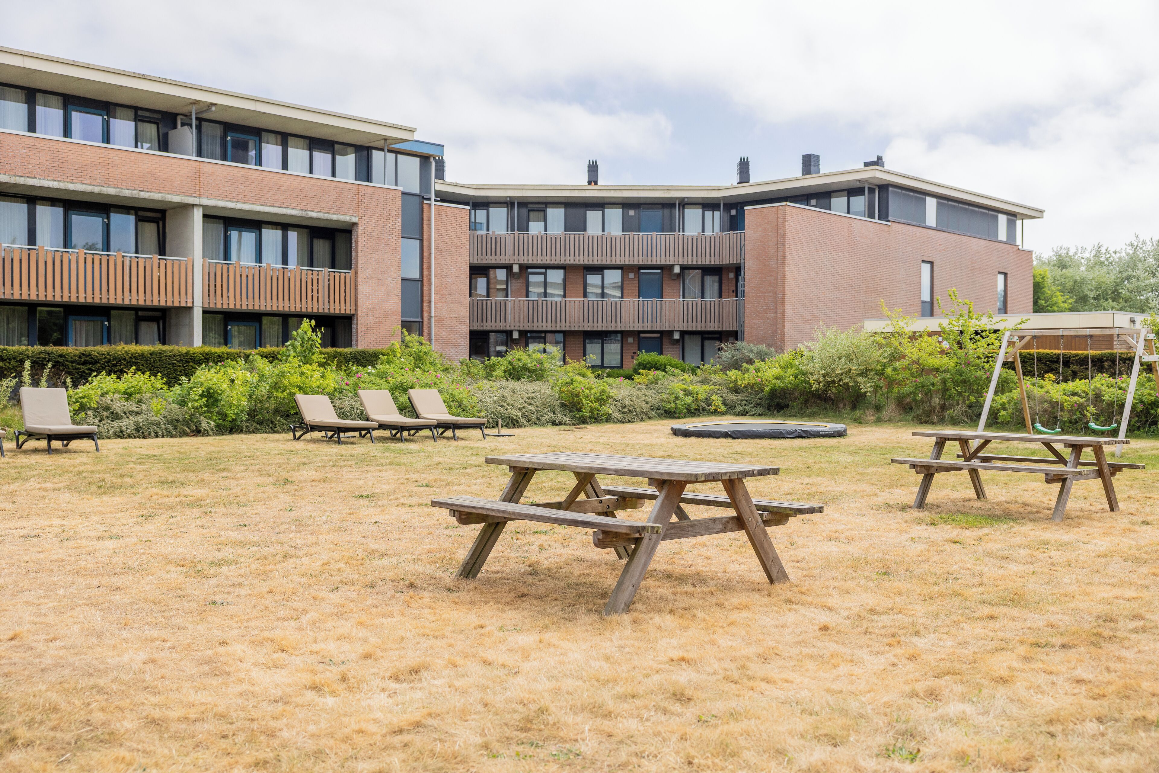 A modern building with multiple balconies, a grassy courtyard with picnic tables, and lounge chairs.