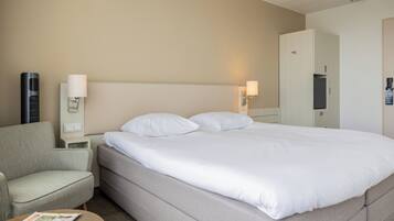 Una habitación de hotel con cama, una silla, mesita de noche, lámpara y armario.