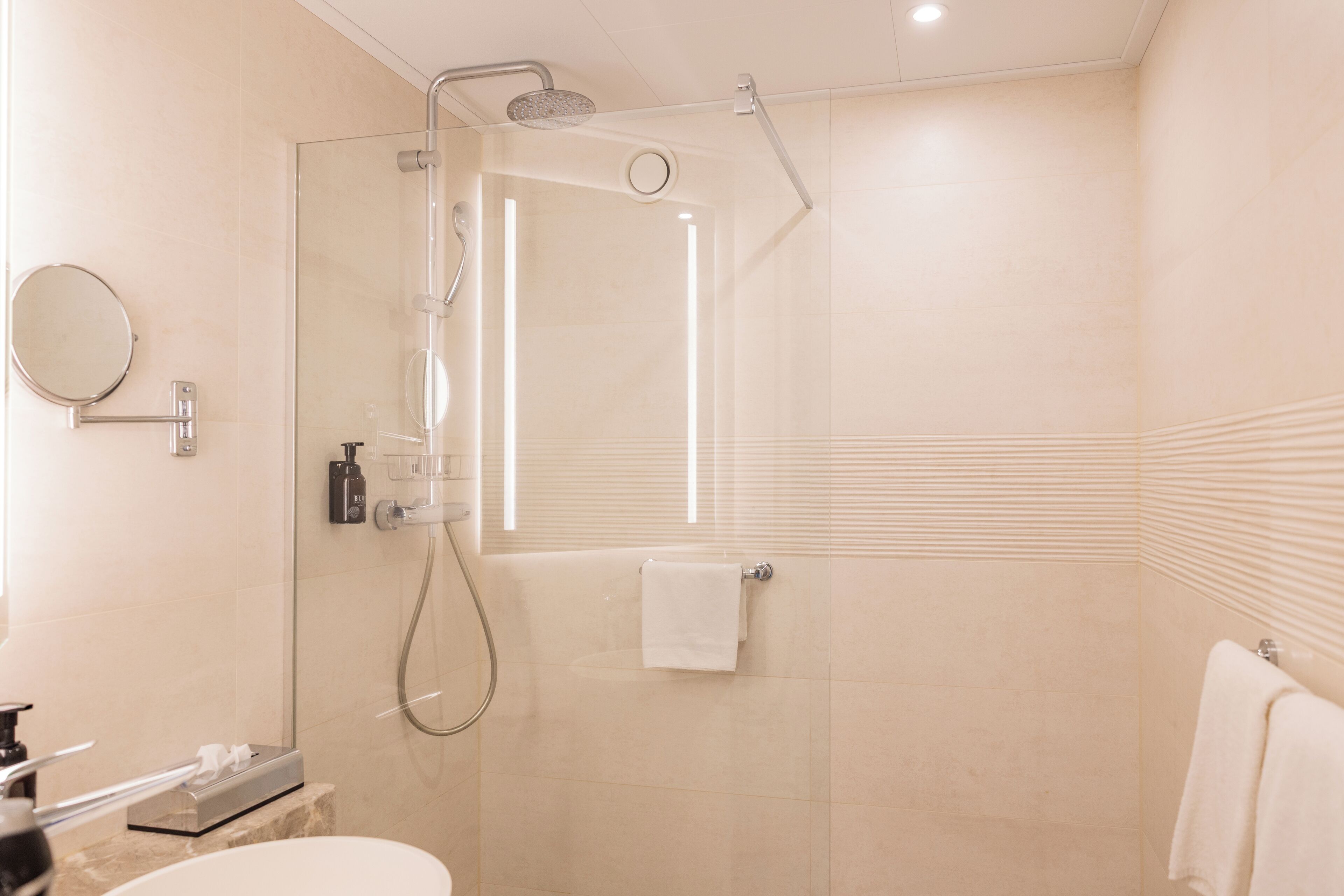 A modern bathroom with a glass-enclosed shower, a round mirror, and a white sink.
