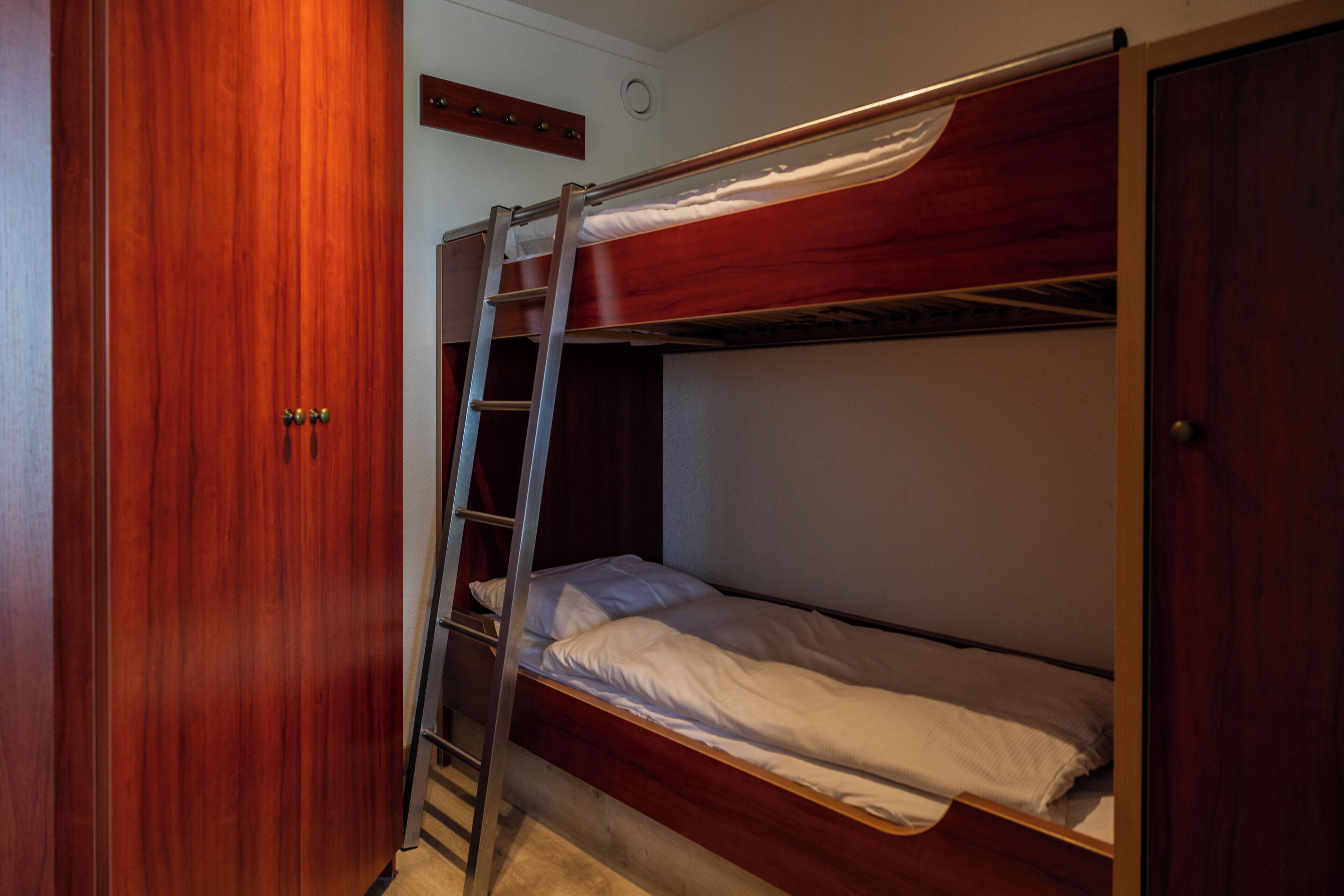 Habitación con literas, un armario de madera y una escalera.