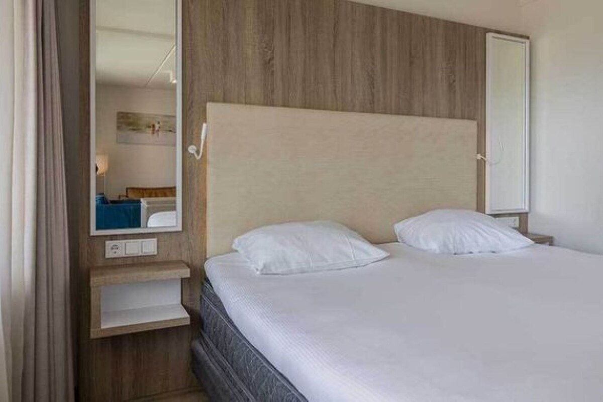 Ein Hotelzimmer mit einem Bett, einem Nachttisch, einem Spiegel und einem hölzernen Kopfteil.