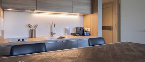 A modern kitchen with wooden cabinets, a stainless steel sink, and a coffee machine.