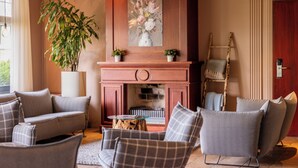 Een woonkamer met een open haard, banken, een bijzettafeltje en een potplant.