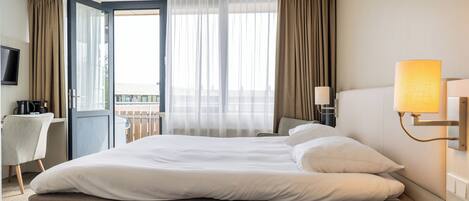 A hotel room with a bed, a desk, a chair, a TV, and a balcony with curtains.