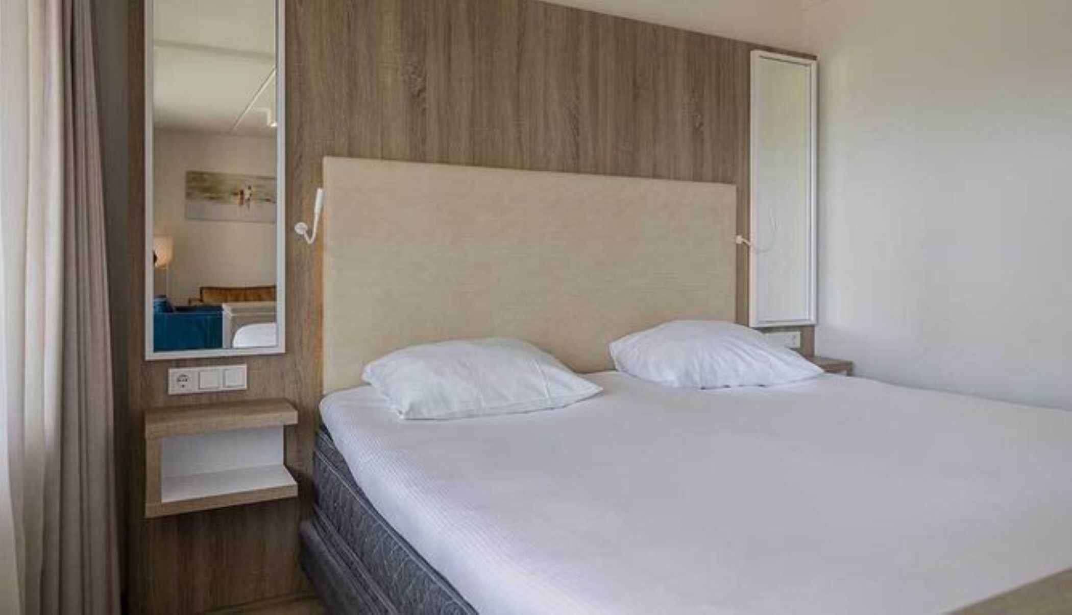 Une chambre d’hôtel avec un lit, une table de chevet, un miroir et une tête de lit en bois.