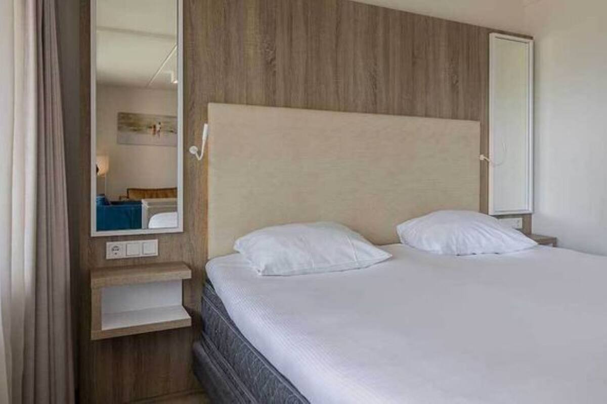 A hotel room with a bed, a nightstand, a mirror, and a wooden headboard.