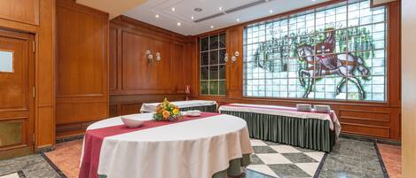 Un salón de conferencias con paneles de madera, un amplio ventanal de vitrales y suelo a cuadros.