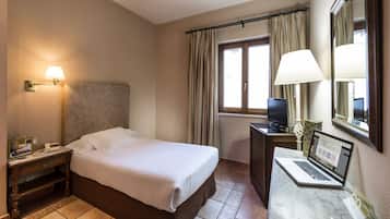 A hotel room with a bed, a desk with a laptop, a television, and a nightstand with a lamp.