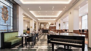 A spacious hotel lobby with a grand piano, dining tables, and a stained glass window. - Dorma Alfonso VIII (Plasencia)