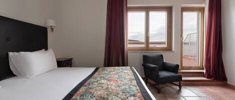 A hotel room with a bed, a chair, a window, and a view of the outside.