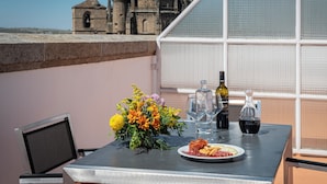 A table with a plate of food, a bottle of wine, and a vase of flowers on a balcony with a view of a historic building. - Dorma Alfonso VIII (Plasencia)