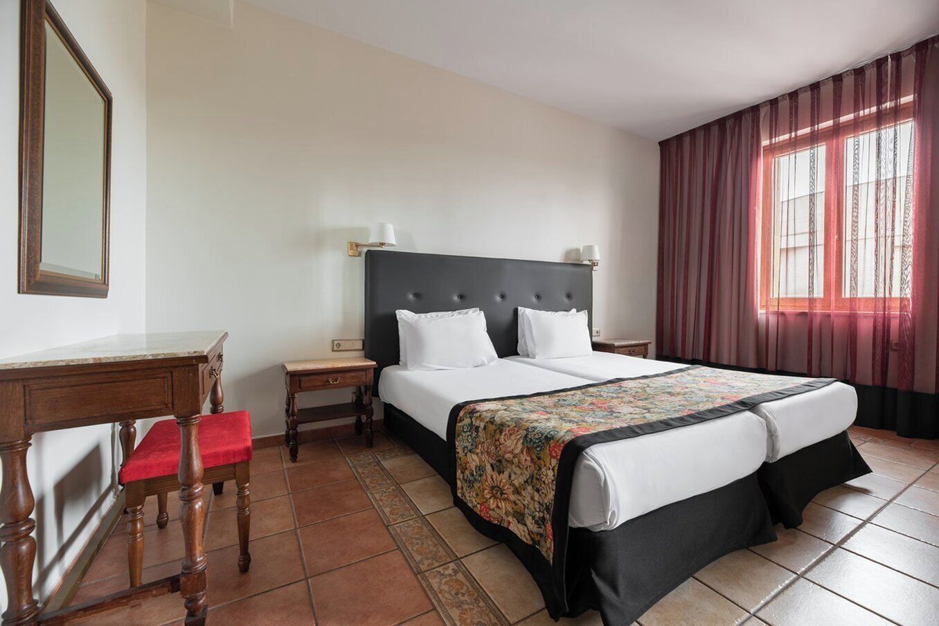 A hotel room with a large bed, a desk, a chair, and a mirror.