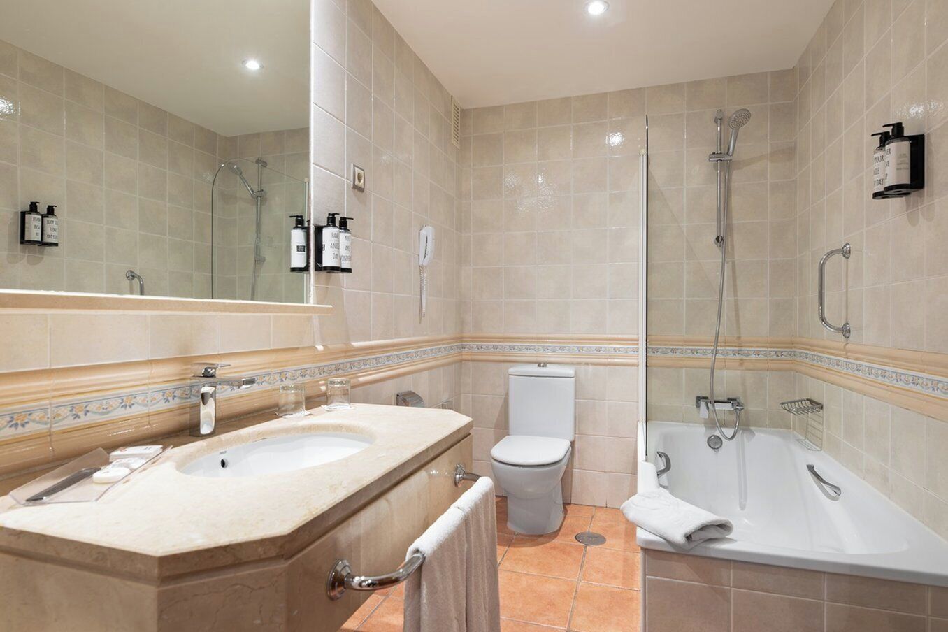 Un baño moderno con tocador doble, inodoro, bañera y zona de ducha con mampara de vidrio.