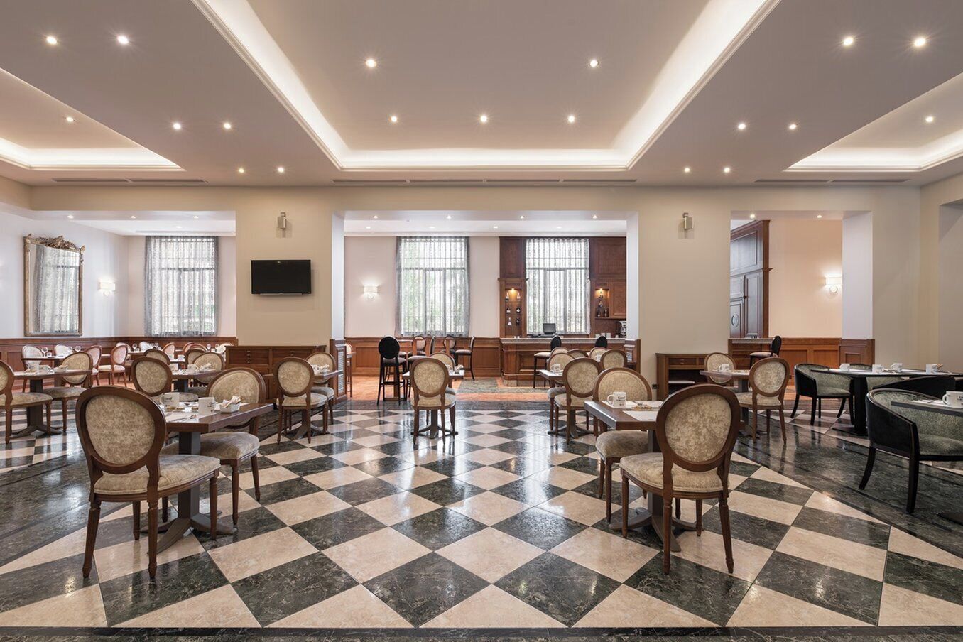 A spacious dining area with checkered flooring, multiple tables and chairs, and a central kitchen area.
