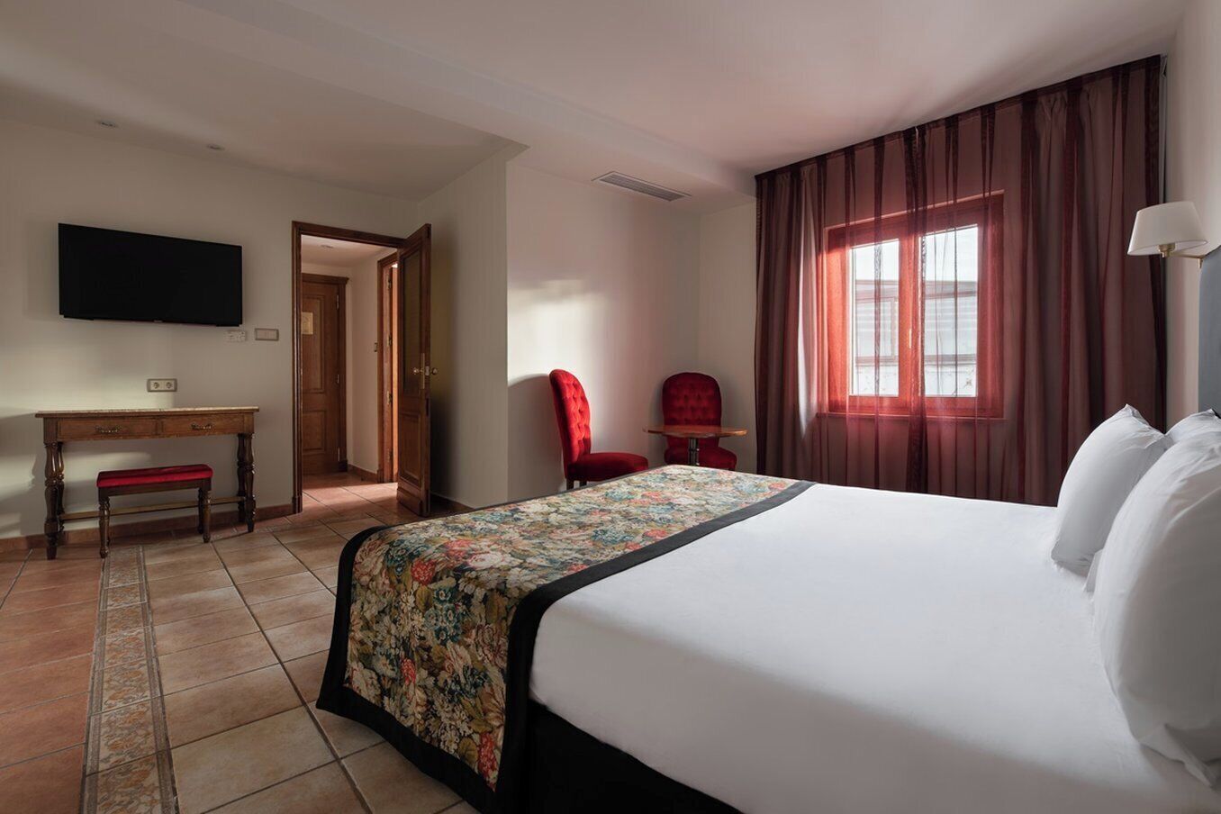 A hotel room with a large bed, a desk with a chair, a television, and a window with curtains.