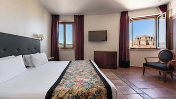 Habitación de hotel con cama, televisor, una silla y ventana con vista a un edificio.