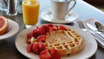 A breakfast setting with waffles topped with strawberries, a glass of orange juice, and a cup of coffee on a table.